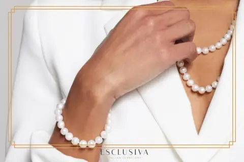 Dłoń w białej marynarce dotyka naszyjnika i bransoletki z pereł. Ich subtelne piękno podkreśla elegancję, ukazując niezwykłe perły właściwości.